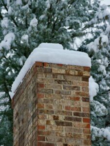 Homeowner inspecting a snow-covered roof from the ground beside clear gutters and trimmed tree branches.
